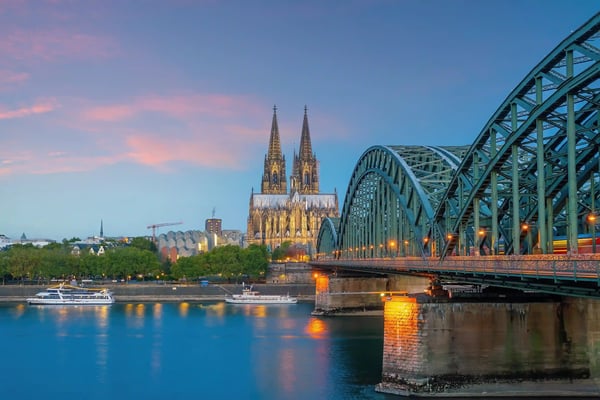 Abendblick auf den Kölner Dom hinter der Hohenzollernbrücke, Lichter spiegeln sich im Rhein, Boote auf dem Fluss.