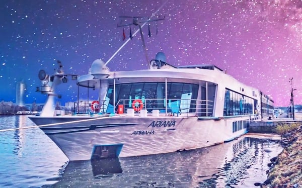 Modernes Flusskreuzfahrtschiff MS Ariana liegt bei Nacht am Ufer vor beleuchtetem Himmel und spiegelt sich im ruhigen Wasser