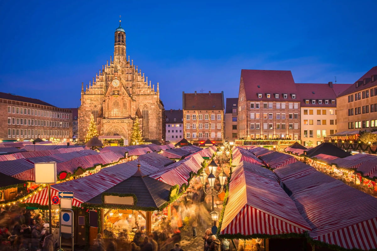 Vue d ensemble du marche de Noel tres frequente de Nuremberg avec stands rayes rouge et blanc et eglise illuminee a l arriere plan