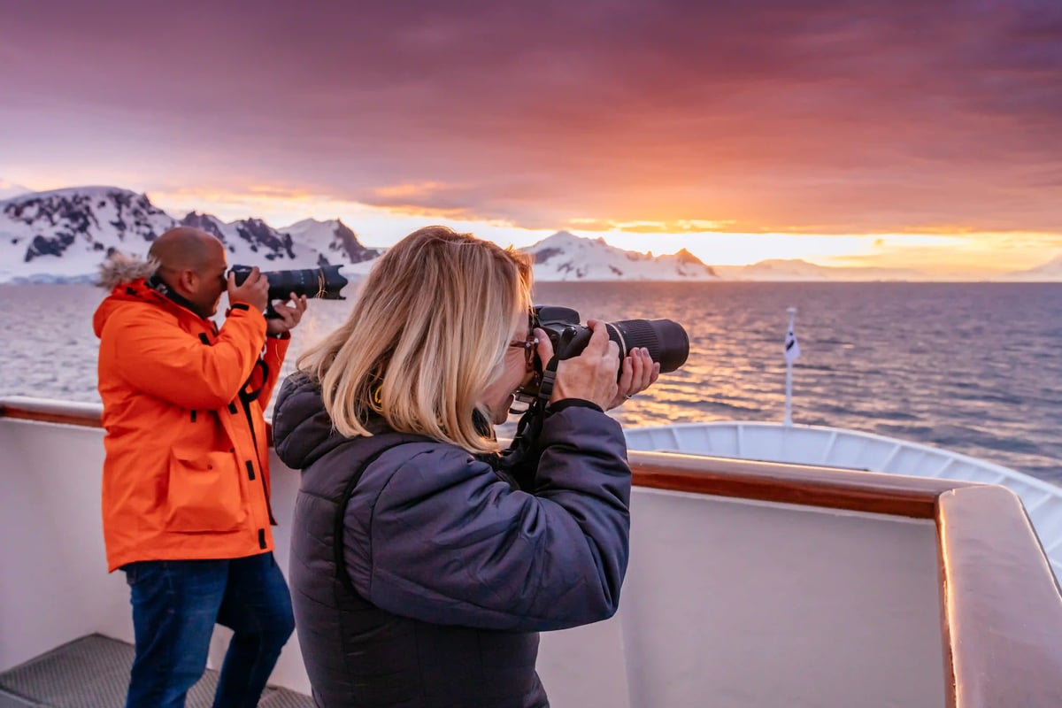 Zeit für EntZwei Personen fotografieren eine küstennahe Polarlandschaft vom Deck eines Schiffes bei warmem Abendlichtdeckungen