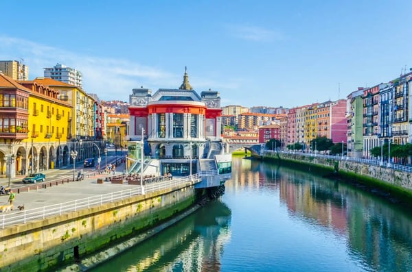 Blick auf die Markthalle von Bilbao am Fluss Nervión mit bunten Häuserfassaden und Spiegelungen im Wasser