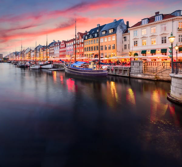 Blick auf den Hafen von Kopenhagen mit bunten Häusern, Booten und Spiegelungen im Wasser bei Abendlicht
