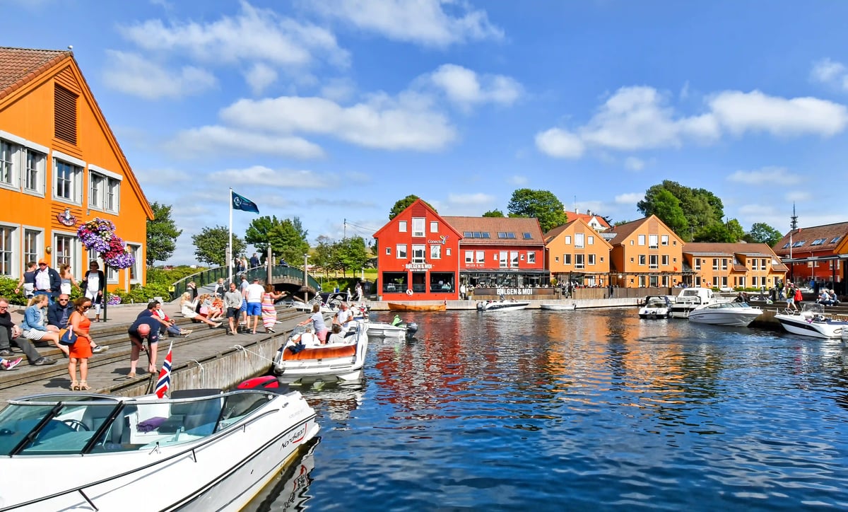 Hafenpromenade in Kristiansand mit bunten Holzhäusern, Booten und Menschen an einem sonnigen Tag