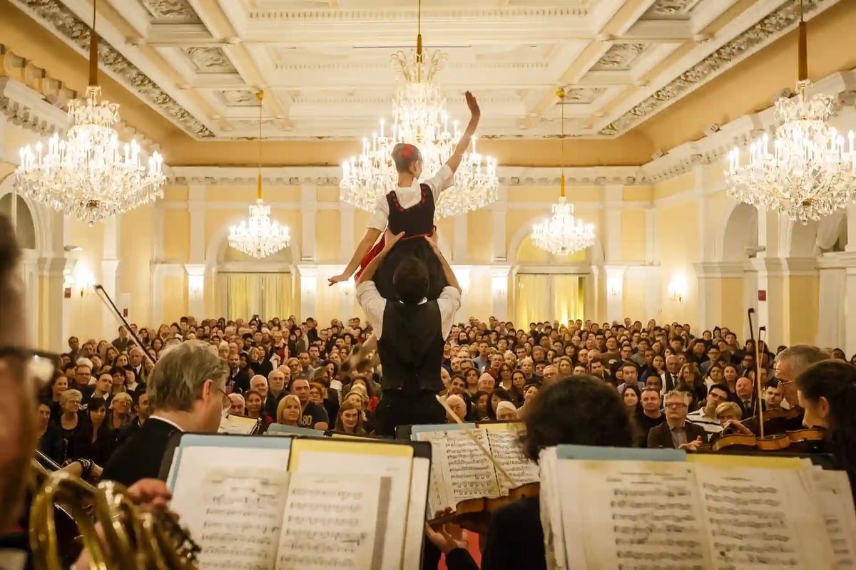Tanzpaar in traditioneller Kleidung bei festlichem Silvesterkonzert vor grossem Publikum im prunkvollen Saal