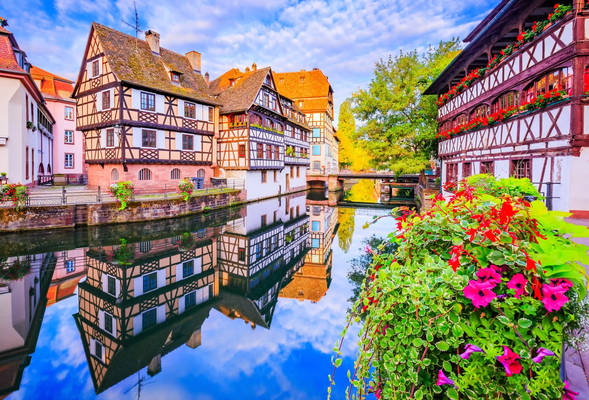 Kanal in Strassburg mit Fachwerkhäusern, Blumen im Vordergrund und Spiegelungen im ruhigen Wasser