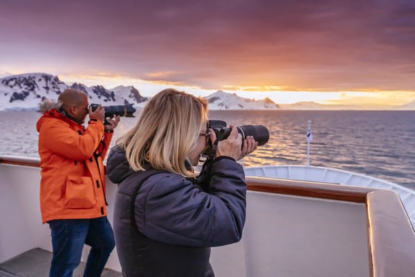 Zwei Personen fotografieren Eislandschaft vom Deck eines Kreuzfahrtschiffs bei Sonnenuntergang