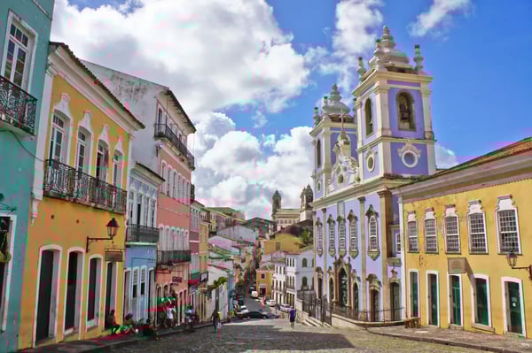 Kopfsteingasse in der Altstadt von Salvador mit bunten Kolonialhäusern und einer barocken Kirche unter blauem Himmel