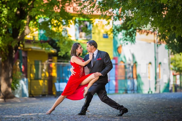 Elegant gekleidetes Tango Tanzpaar in enger Tanzpose auf einer Strasse mit bunten Haeusern im Hintergrund