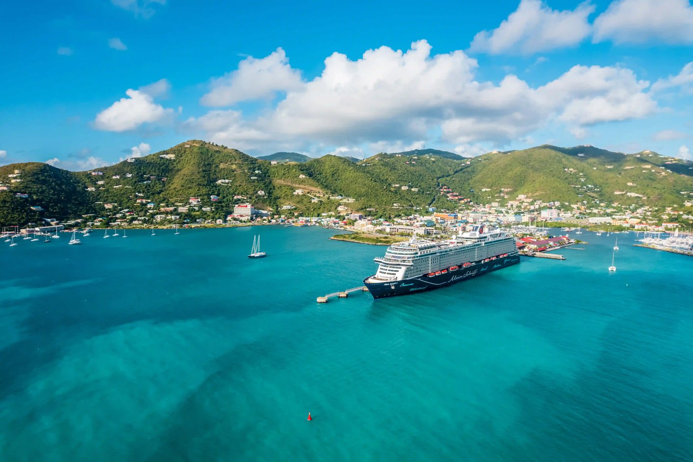 Kreuzfahrtschiff im Hafen mit tuerkisfarbenem Meer, Anlegesteg und gruener Huegellandschaft im Hintergrund