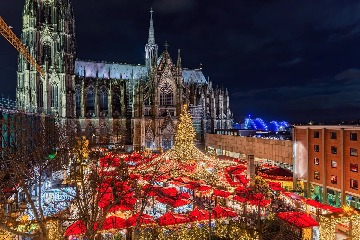 Marché de Noël en soirée avec grande pyramide illuminée, foule et décorations festives.