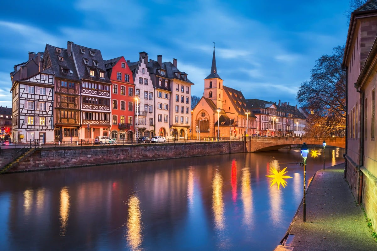 Soir à Strasbourg: maisons à colombages et église au bord du canal, reflets des lumières dans l eau calme.