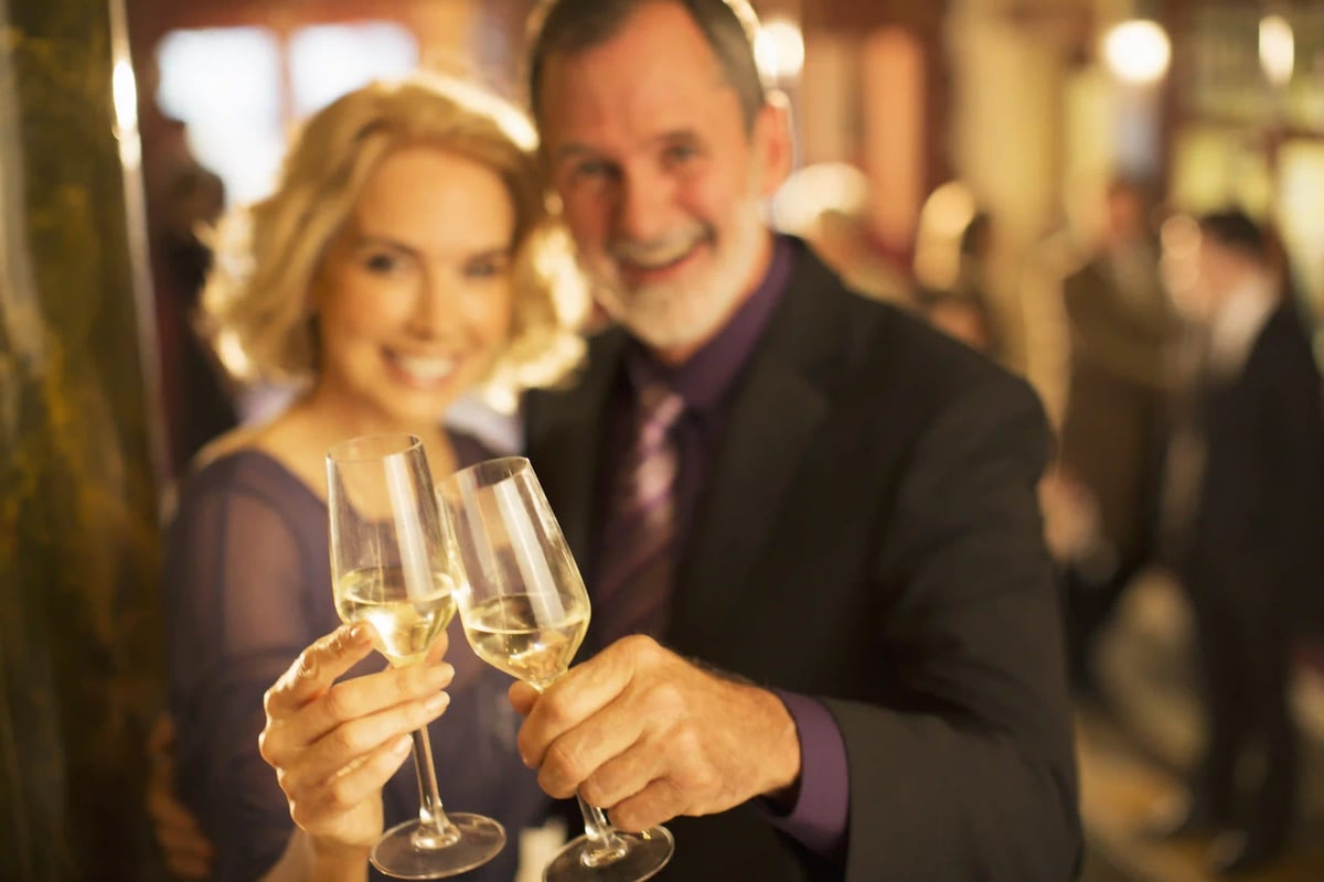 Deux adultes élégamment habillés portent un toast avec des coupes de champagne lors d une réception dans une ambiance chaleureuse et festive.