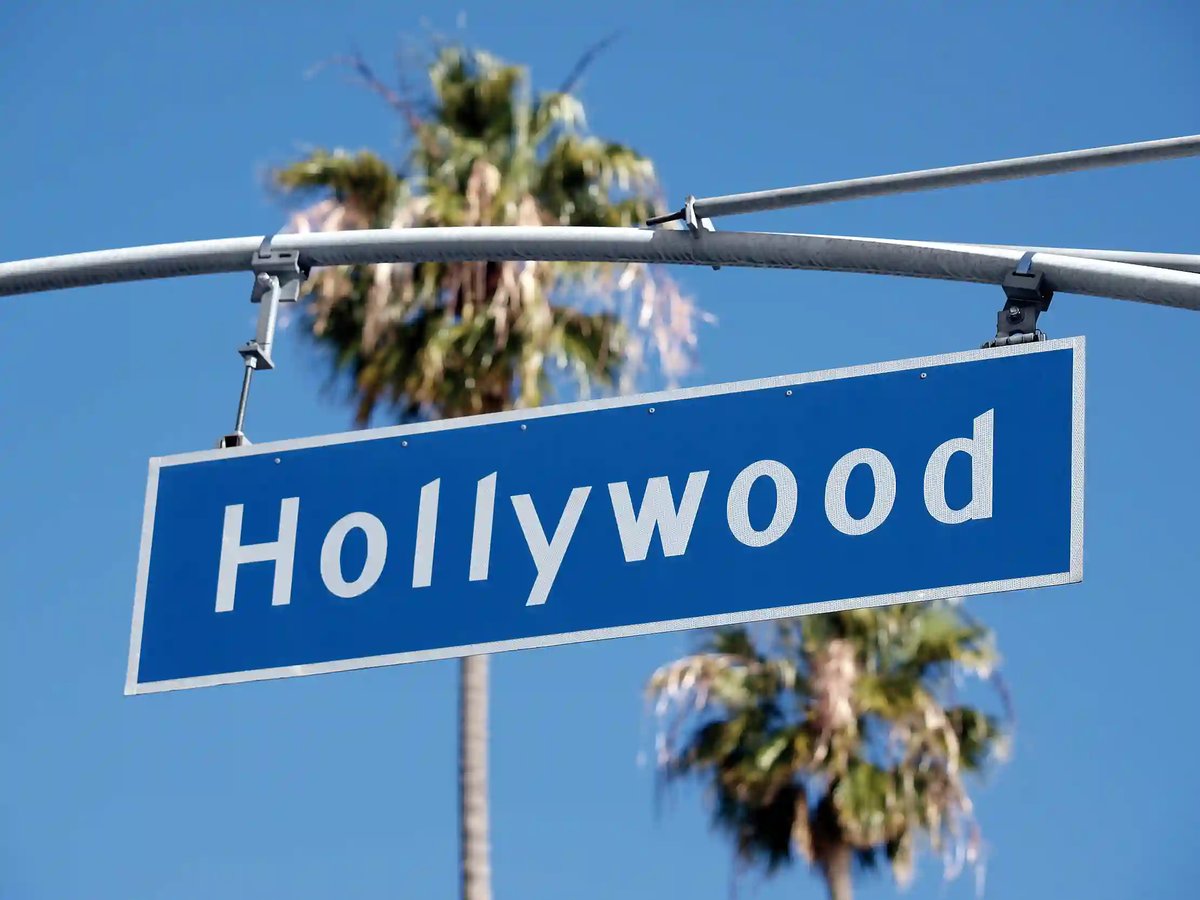 Blaues Strassenschild mit der Aufschrift Hollywood vor Palmen und blauem Himmel