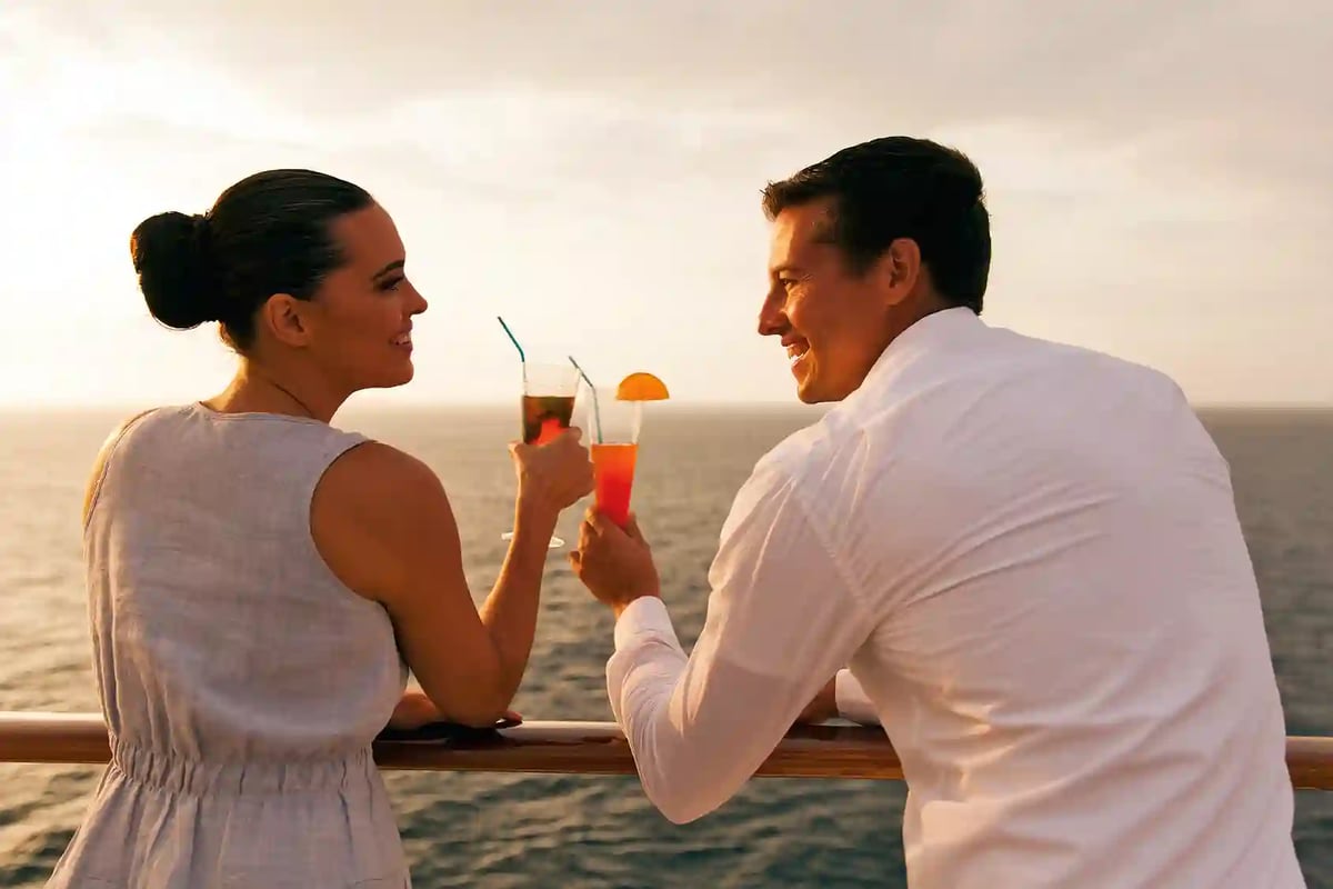 Paar stösst mit Cocktails an der Reling eines Schiffes bei Sonnenuntergang an