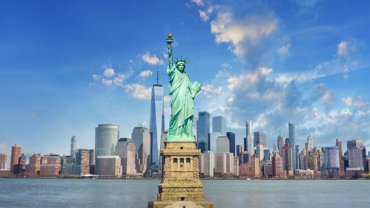 Freiheitsstatue vor Skyline von New York mit Hochhäusern und blauem Himmel