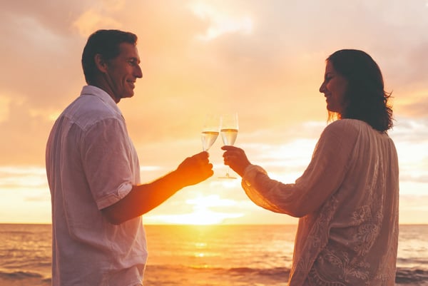 Paar stösst mit Sektgläsern am Strand bei Sonnenuntergang an