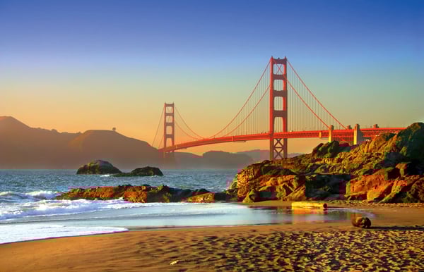 Golden Gate Bridge bei Sonnenuntergang mit Strand, Felsen und Wellen im Vordergrund