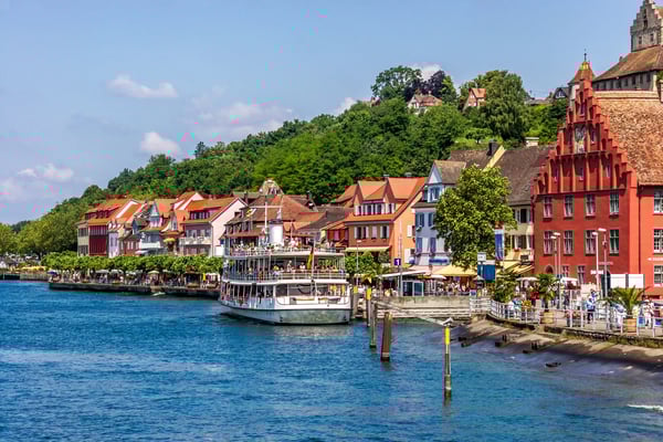 Bateau de passagers sur le lac de Constance, devant une promenade bordée de maisons colorées et de collines verdoyantes.