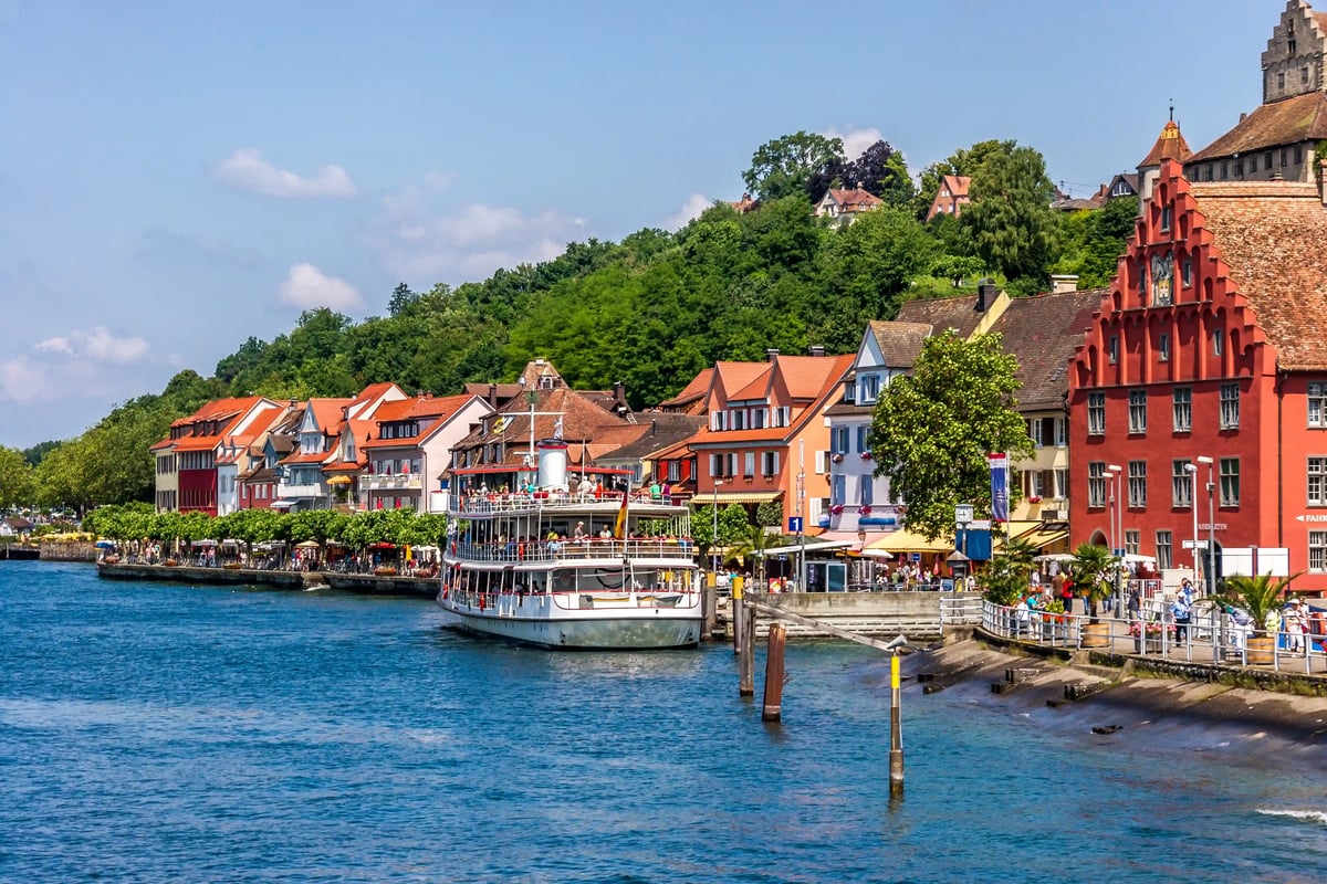 Bateau de passagers sur le lac de Constance, devant une promenade bordée de maisons colorées et de collines verdoyantes.