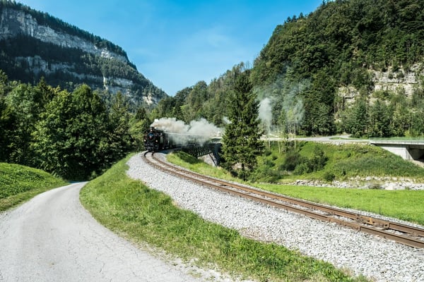 Train à vapeur historique circulant sur une voie ferrée à travers une vallée boisée du Bregenzerwald.