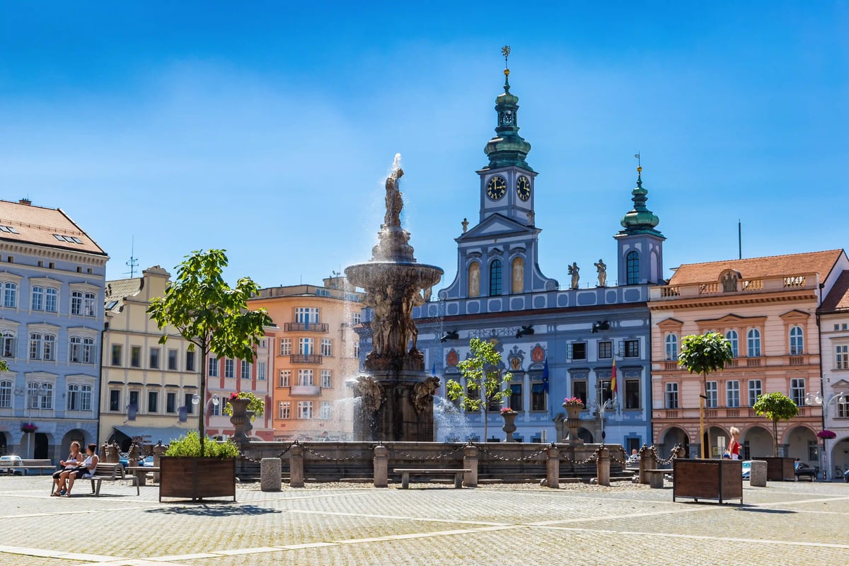 Place principale de České Budějovice avec fontaine baroque centrale, façades historiques et tour de l’hôtel de ville.