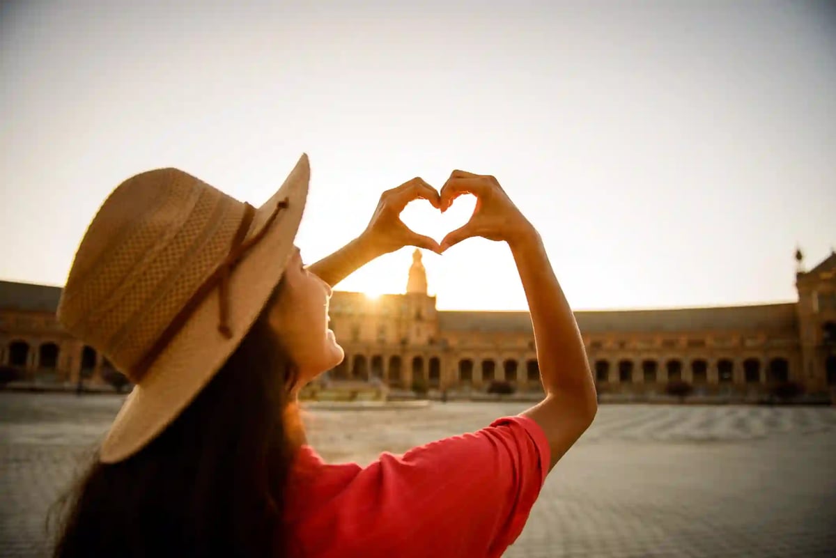 Visiteuse formant un coeur avec ses mains devant une place historique au coucher du soleil