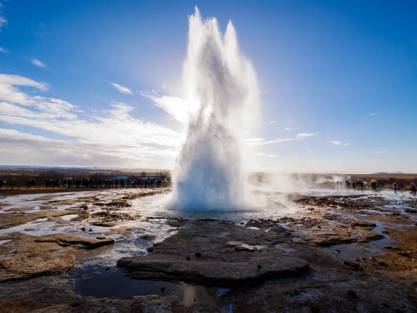 Geyser islandais en éruption projetant une haute colonne d’eau dans un paysage géothermique.