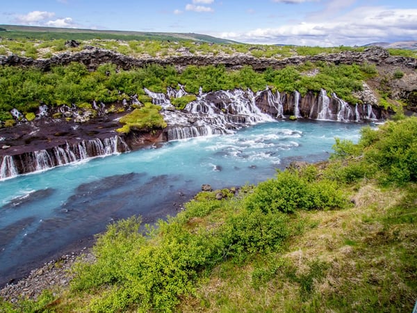 Série de cascades Hraunfossar s’écoulant dans une rivière turquoise à travers un champ de lave.