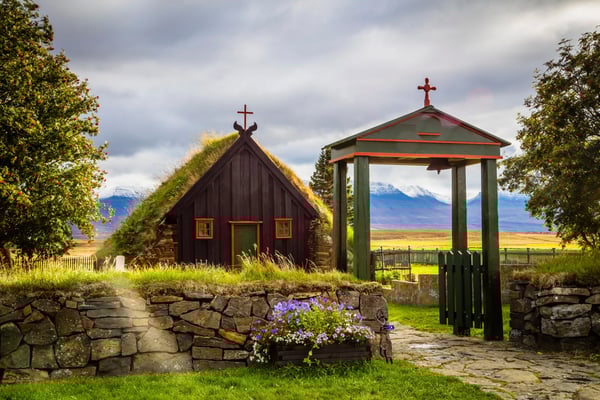 Petite église islandaise traditionnelle en bois avec toit en tourbe, entourée de nature.