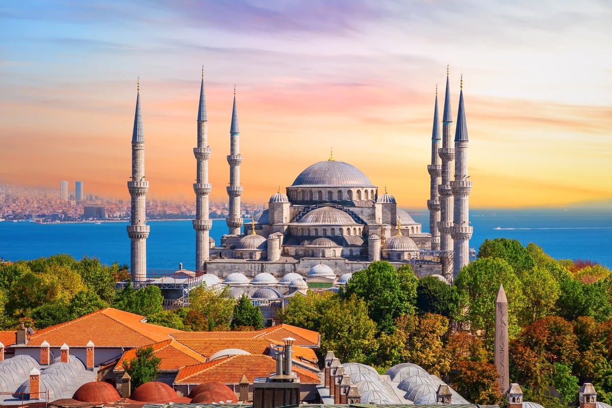 Mosquée Sultan Ahmed à Istanbul avec dôme central et six minarets sous un ciel coloré.