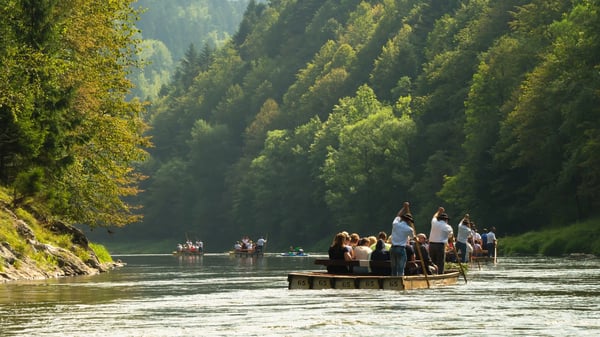 Radeaux en bois transportant des visiteurs sur une rivière, entourée de collines boisées.