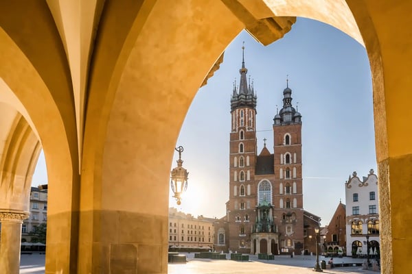 Vue de la basilique Sainte-Marie à Cracovie, encadrée par une arche et éclairée par le soleil.