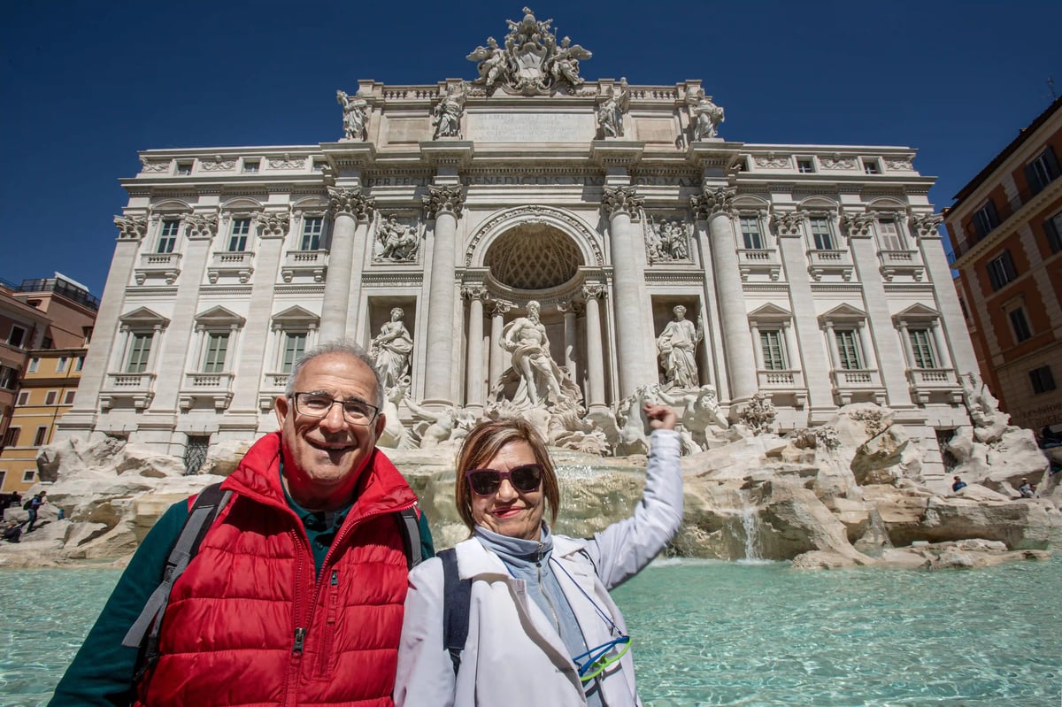 Couple de voyageurs souriant devant la fontaine de Trevi avec façade baroque monumentale