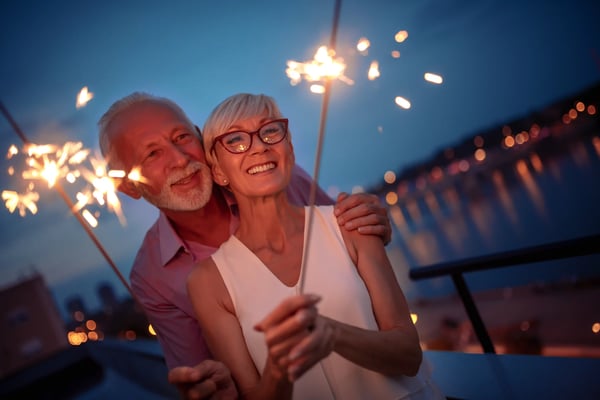 Couple souriant tenant des cierges magiques devant un lac au crépuscule.