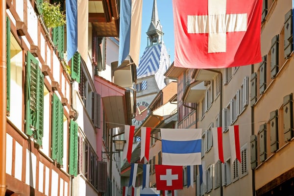 Rue étroite d’une vieille ville suisse décorée de drapeaux nationaux entre maisons traditionnelles.