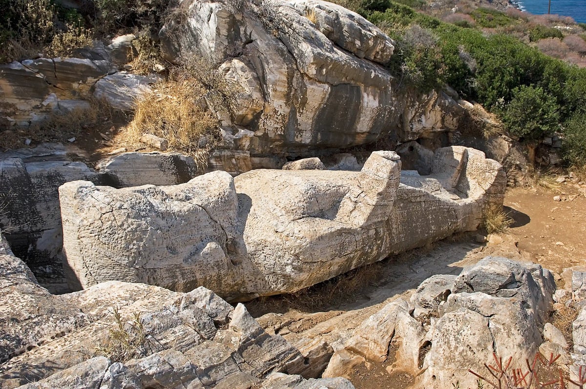Statue antique inachevée du Kouros d’Apollonas allongée dans un paysage rocheux.