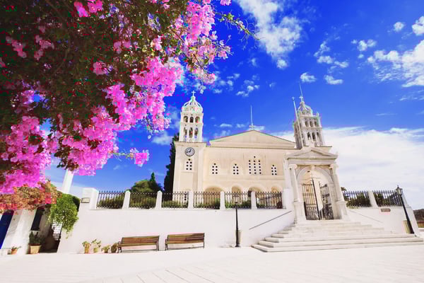 Église blanche traditionnelle entourée de fleurs roses sous un ciel bleu.