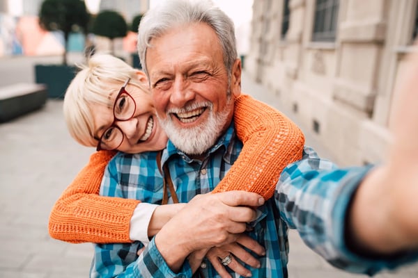 Couple de seniors souriant, enlacé, prenant un selfie en ville.