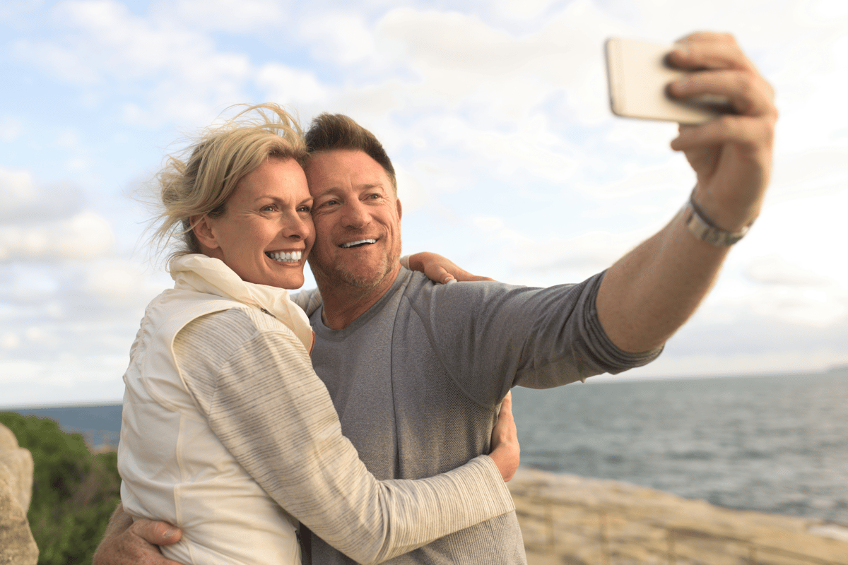 Couple de voyageurs souriant prenant un selfie au bord de la mer.