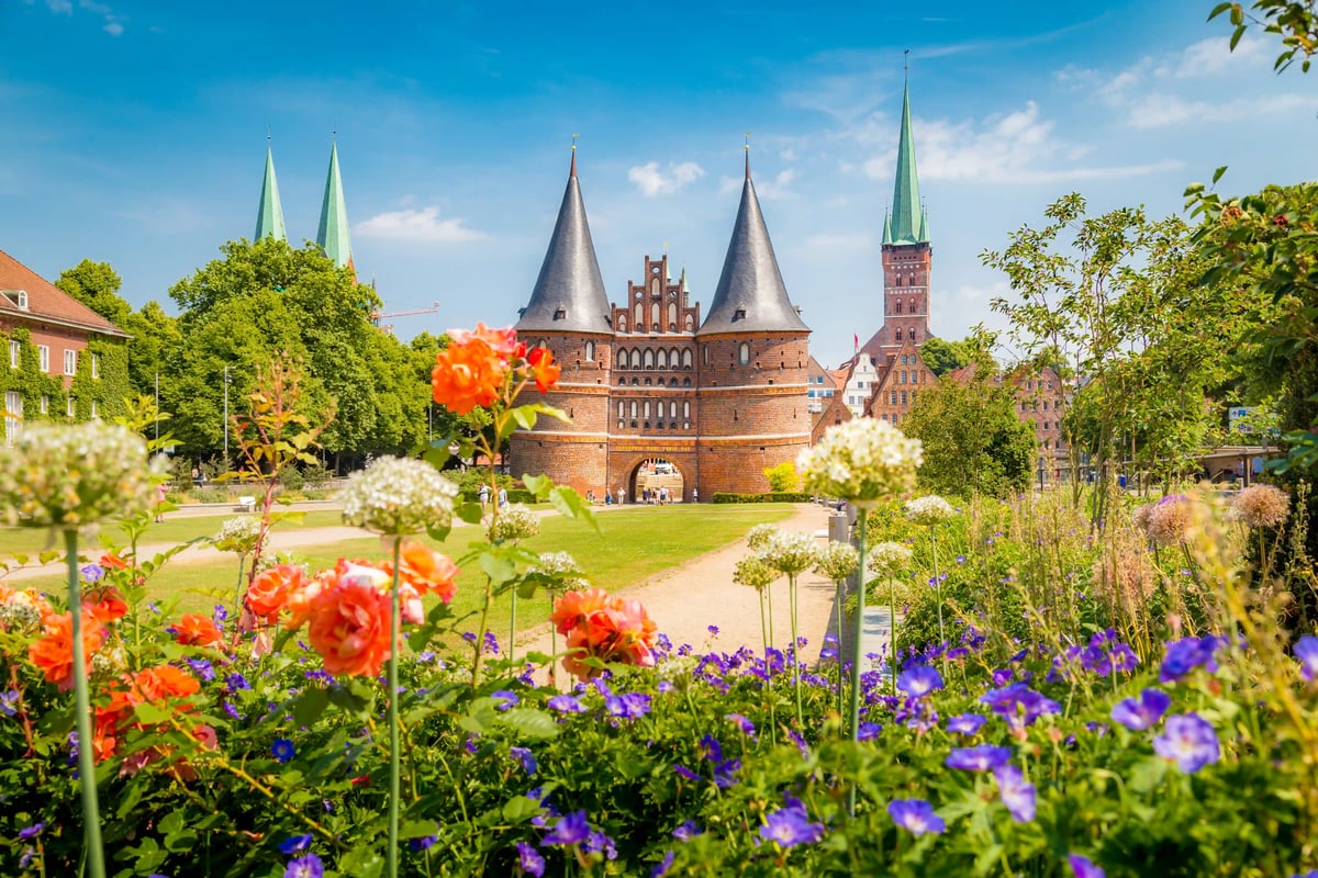 Porte de Holstentor à Lübeck avec parc fleuri et clochers historiques en arrière-plan.