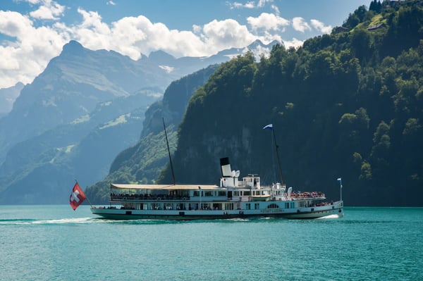 Bateau à vapeur naviguant sur le lac des Quatre-Cantons avec des passagers à bord, entouré de montagnes escarpées et boisées