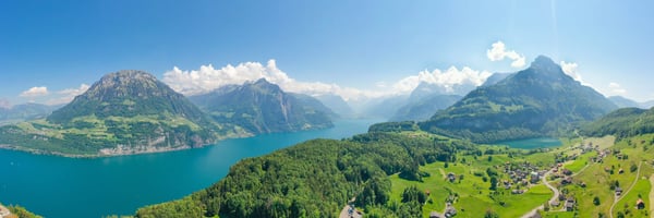 Panorama du lac des Quatre-Cantons avec des montagnes suisses, des forêts vertes et des villages alpins sous un ciel bleu