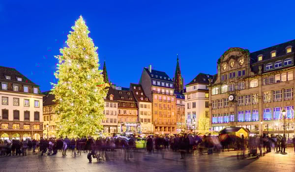 Place centrale de Strasbourg animée avec grand sapin de Noël, foule de visiteurs et illuminations festives en soirée