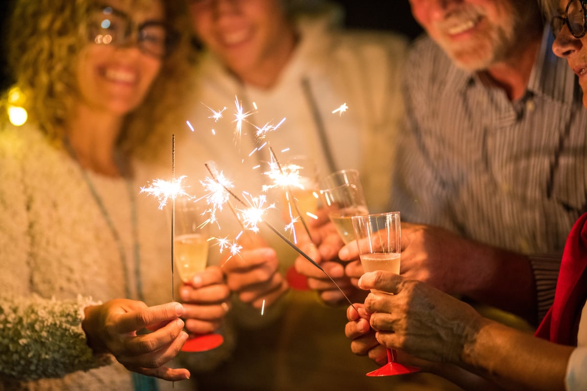 Personnes souriantes tenant des cierges magiques et des verres lors d’une fête conviviale