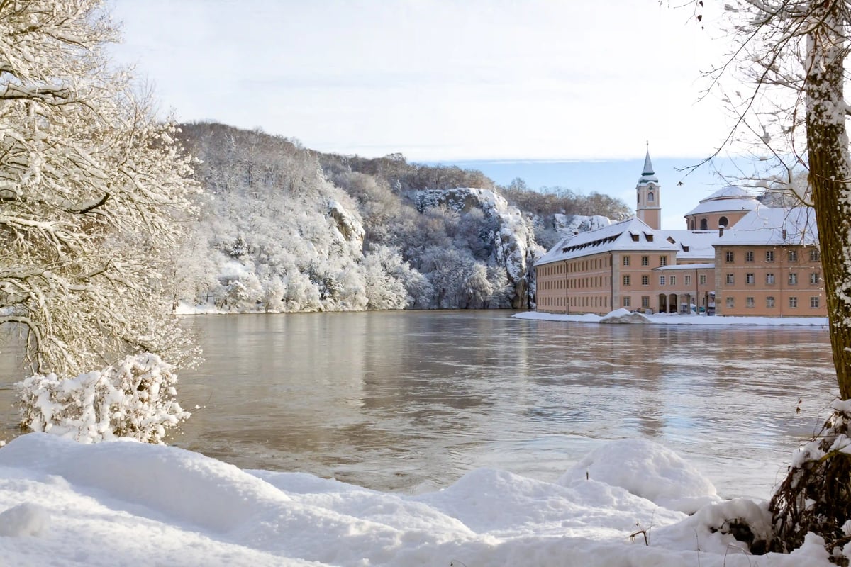Paysage hivernal enneige au bord du Danube avec le monastere de Weltenburg sur la rive et des collines boisees en arriere plan.