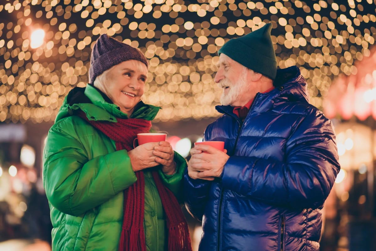 Deux voyageurs ages en vetements d hiver boivent une boisson chaude et discutent devant des illuminations festives.