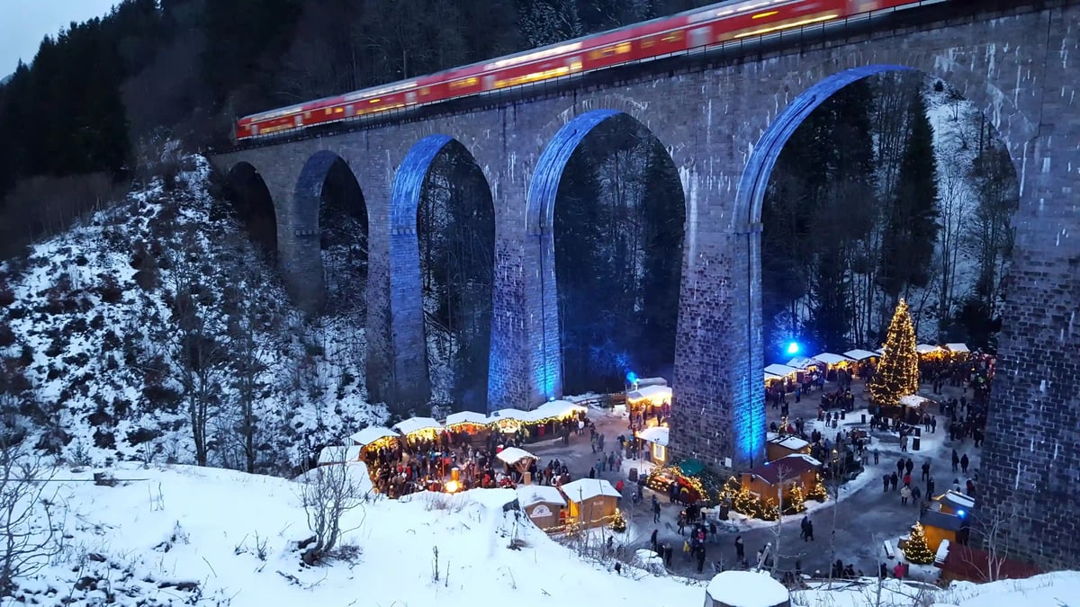 Zug fährt über ein Viadukt oberhalb eines Weihnachtsmarkts in der verschneiten Ravenna-Schlucht