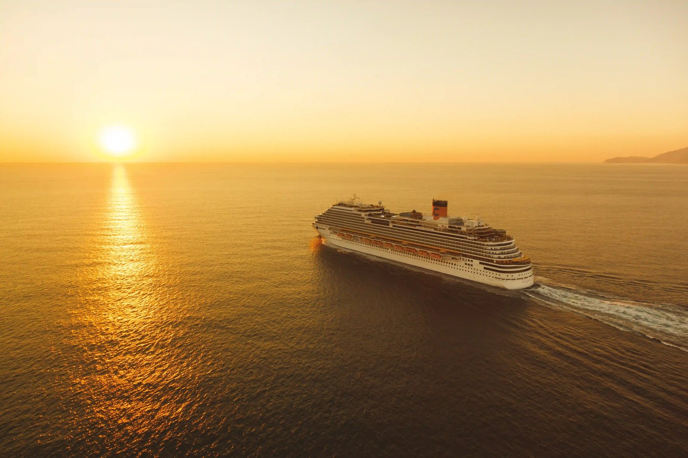 Kreuzfahrtschiff Costa Diadema fährt bei Abenddämmerung auf ruhigem Meer mit Bergen am Horizont