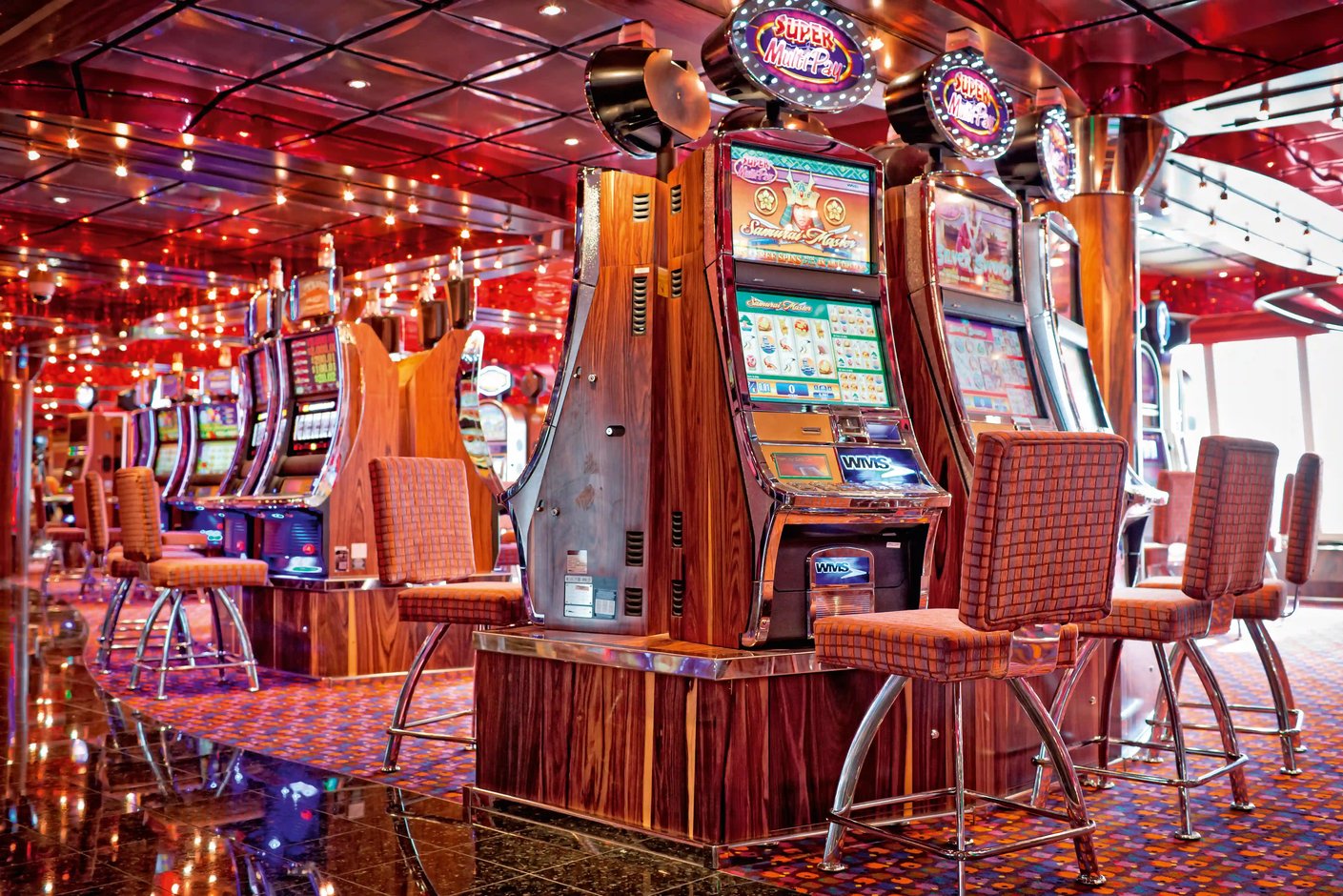 Casino auf der Costa Diadema mit beleuchteten Spielautomaten, gepolsterten Sitzhockern, glänzendem Boden und roter Deckenbeleuchtung