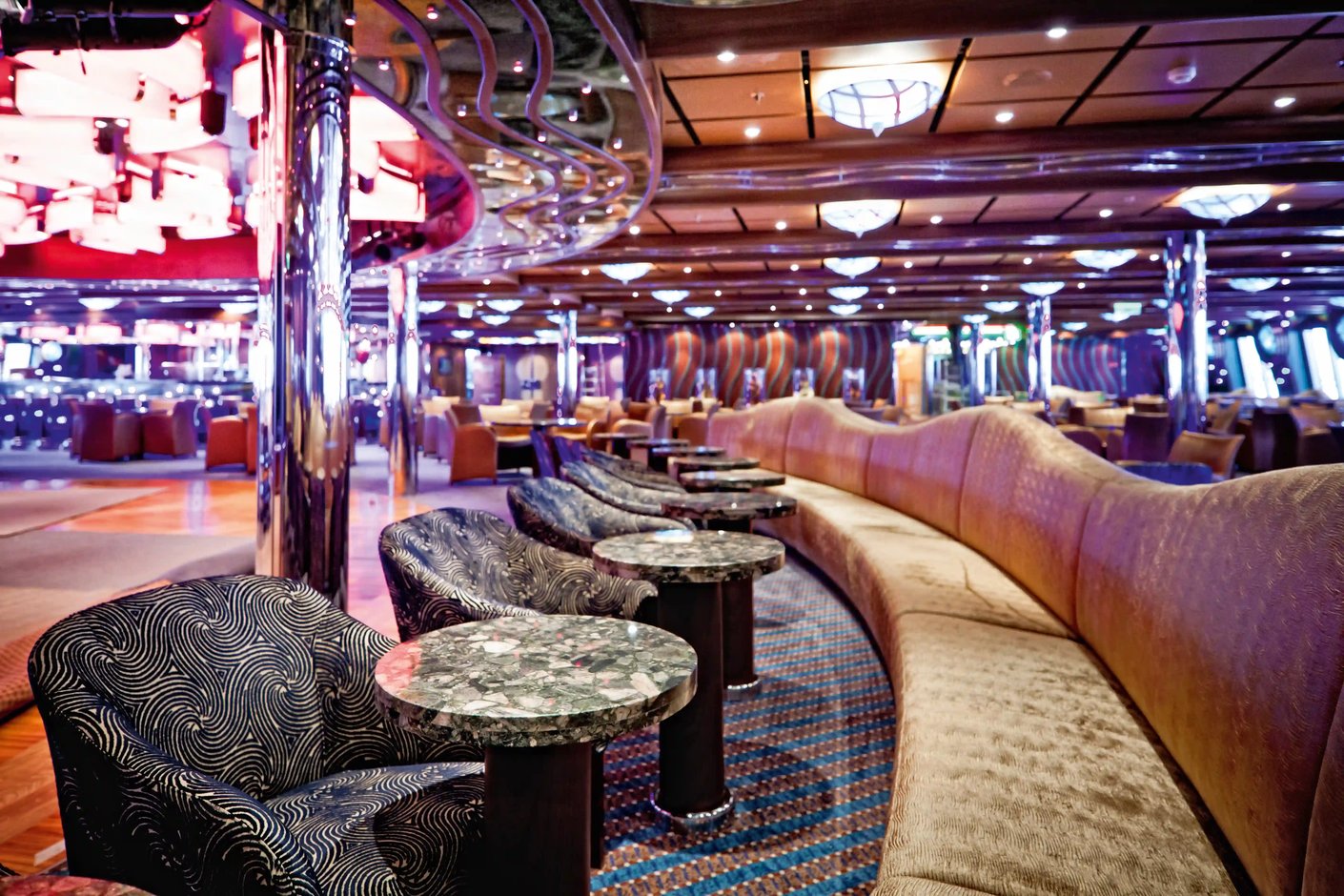 Grosszügige Lounge mit geschwungenen Sofas, kleinen Tischen und dekorativer Beleuchtung